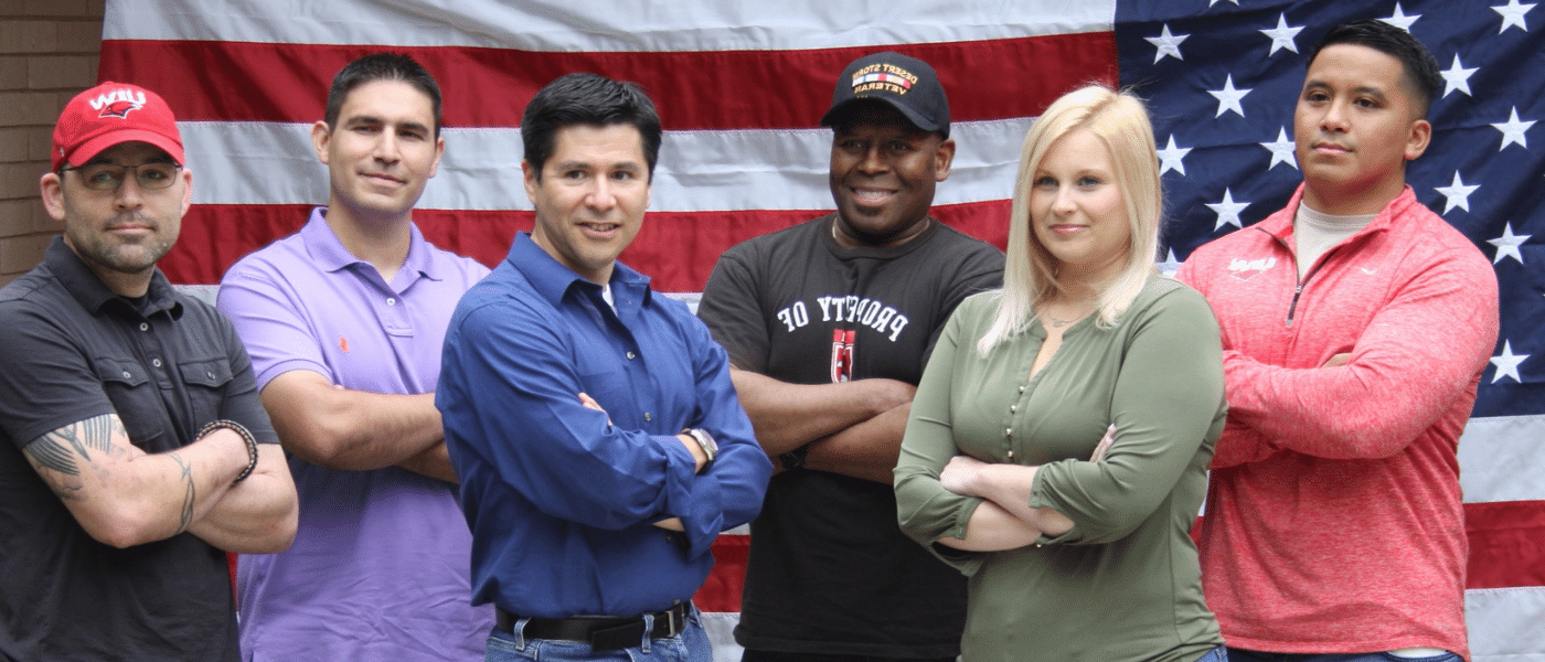 Group of veteran students standing in front of the U.S. flag with their arms crossed.